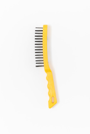 Una spazzola di filo di acciaio con una maniglia gialla brillante che giace sul semplice sfondo bianco