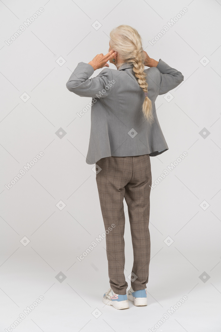 Vista trasera de una anciana en traje de pie con las manos detrás de la cabeza