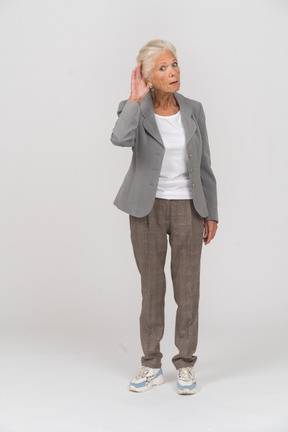 Vista frontal de una anciana en traje mirando a la cámara y escuchando atentamente
