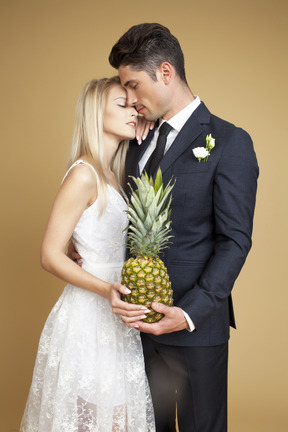 Bride and groom standing shoulder to shoulder and holding a pineapple