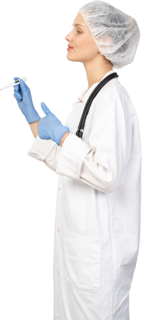 Vista lateral de una joven doctora con estetoscopio sosteniendo el termómetro y mostrando el pulgar hacia arriba