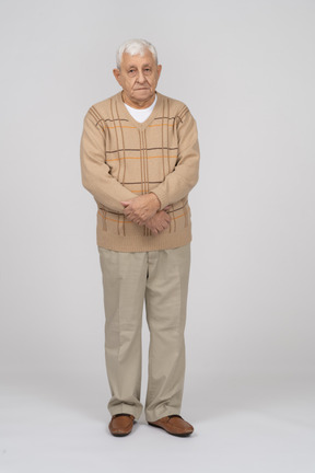Front view of an old man in casual clothes standing with crossed hands