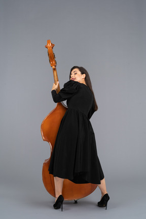 Back view of a pleased young female musician in black dress holding her double-bass