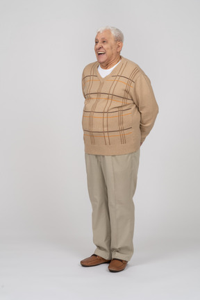 Vorderansicht eines glücklichen alten mannes in freizeitkleidung, der mit den händen nach hinten steht