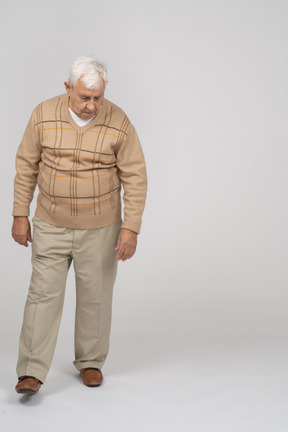 Front view of an old man in casual clothes walking and looking down