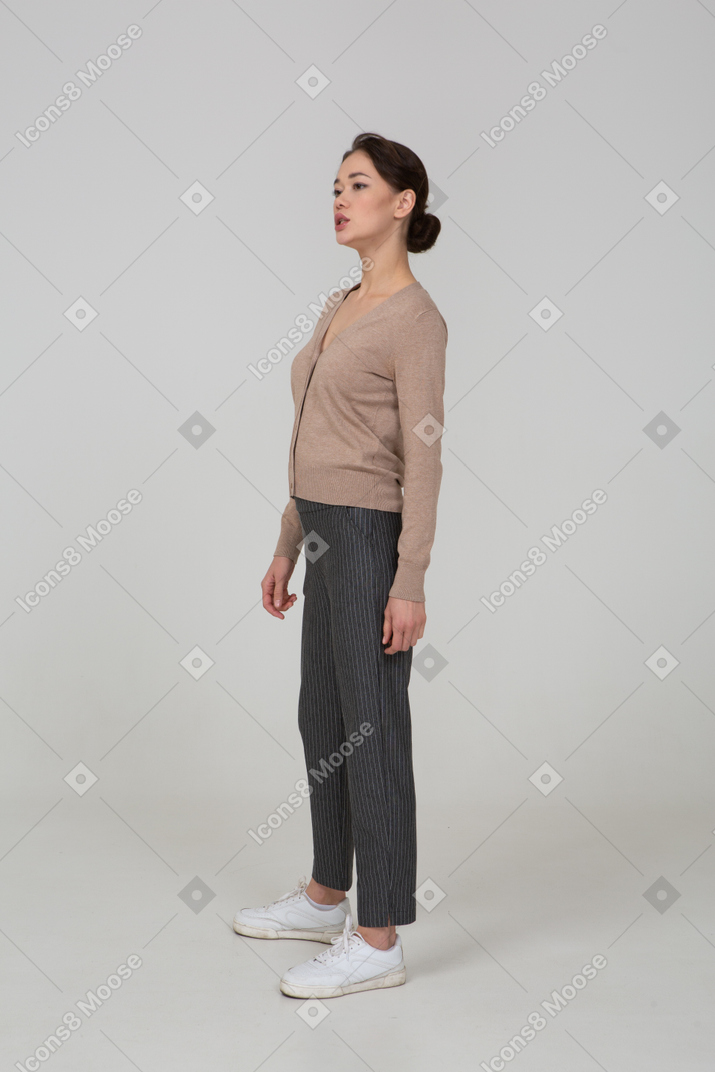 Vista di tre quarti di una giovane donna in piedi ancora in pullover e pantaloni che guarda da parte