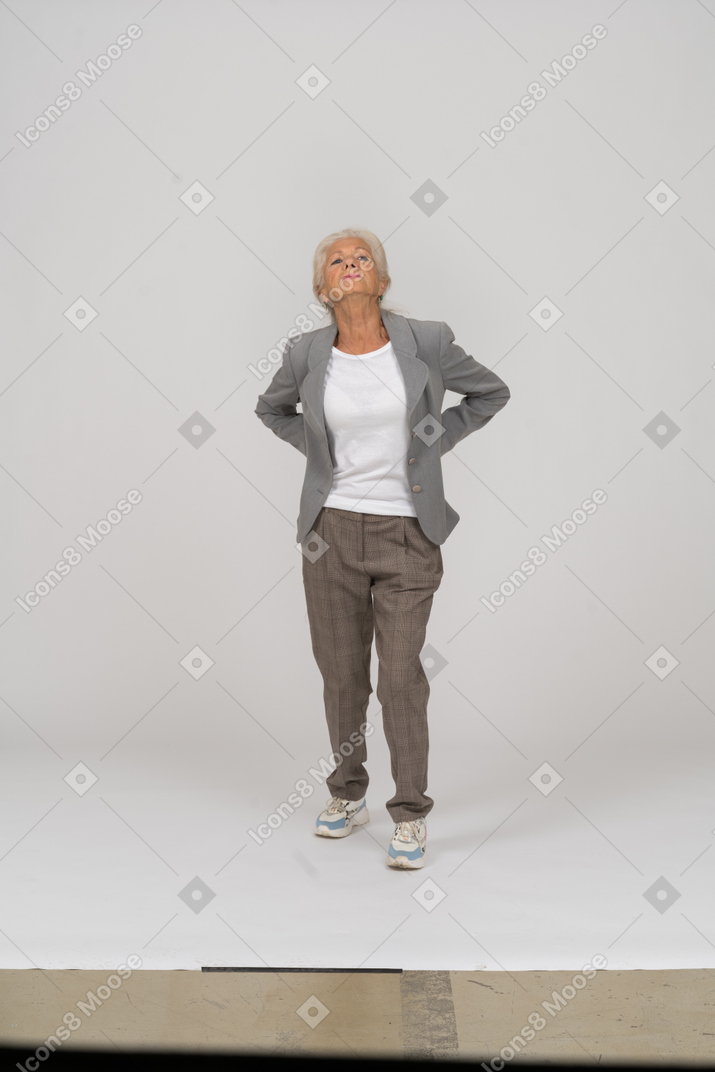 Vorderansicht einer alten dame im anzug, die mit den händen hinter dem rücken steht und nach oben schaut