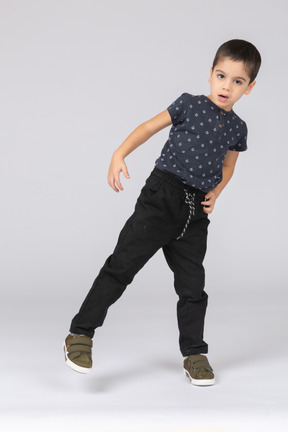 Вид спереди симпатичного мальчика, балансирующего на одной ноге и смотрящего в камеру