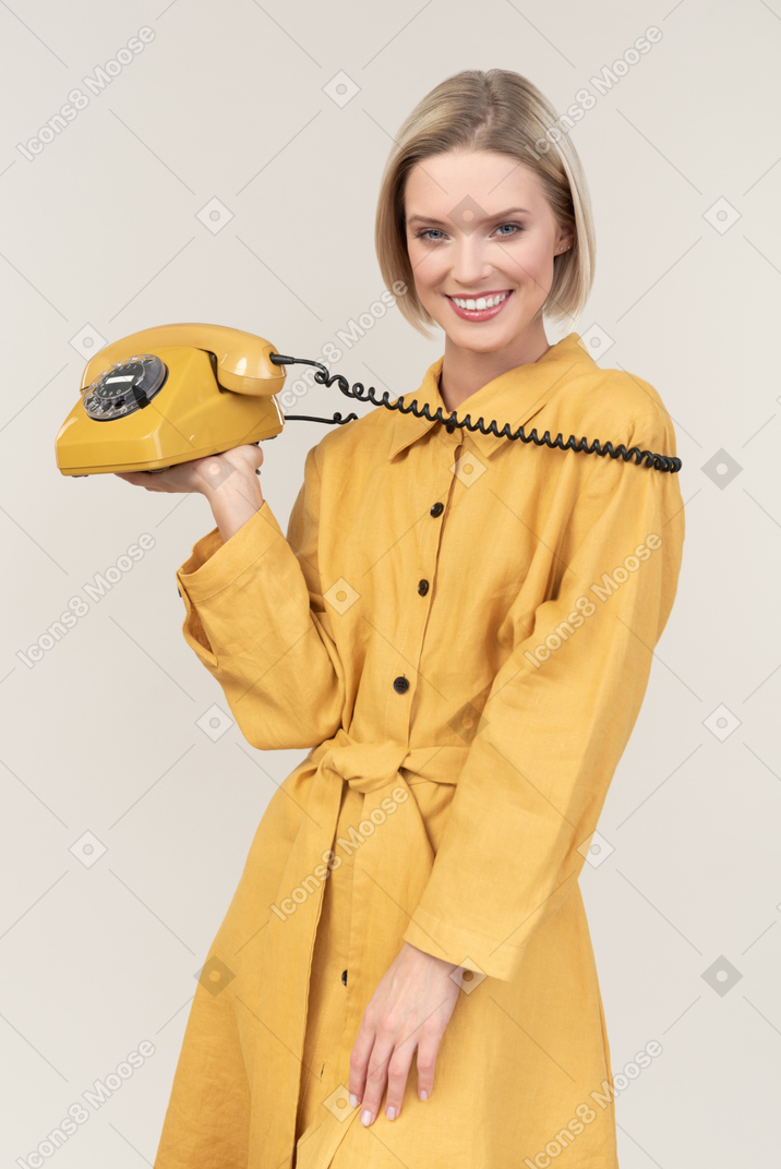 Smiling young woman holding vintage phone's cord over shoulders