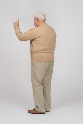 Vista lateral de un anciano con ropa informal apuntando hacia arriba con un dedo