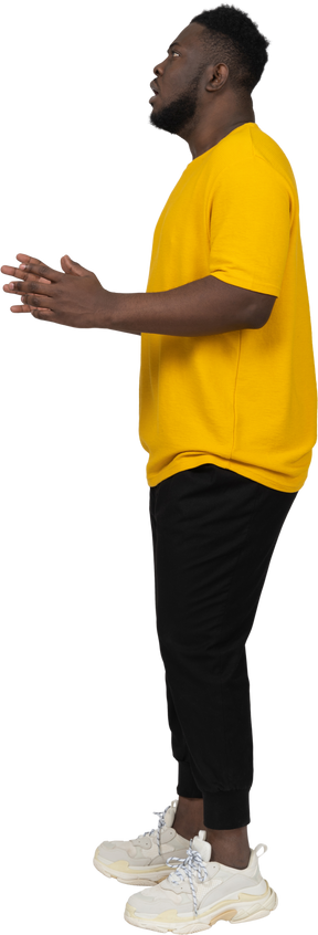 Side view of a young shocked dark-skinned man in yellow t-shirt raising hands