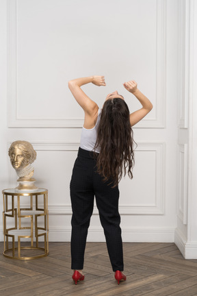 Vista posteriore di una giovane donna alzando le mani e gettando la testa indietro mentre si trovava vicino a una scultura greca dorata