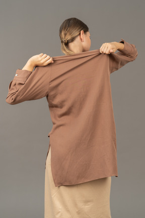 Вид сзади на женщину, снимающую рубашку двумя руками