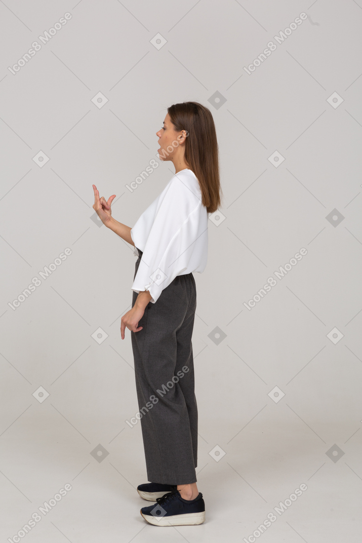 Side view of a young lady in office clothing showing rock gesture