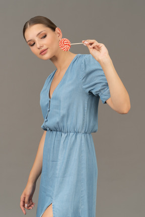 ロリポップを保持している青いドレスを着た若い女性の4分の3のビュー