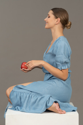 Side view of young woman with apple sitting on cube