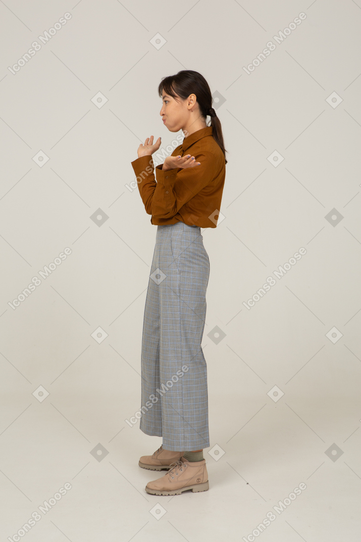 Side view of a funny young asian female in breeches and blouse raising hands