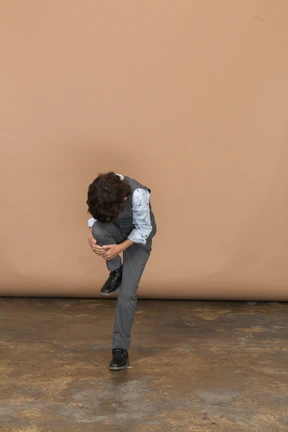 Front view of a boy in grey suit suffering from pain in leg