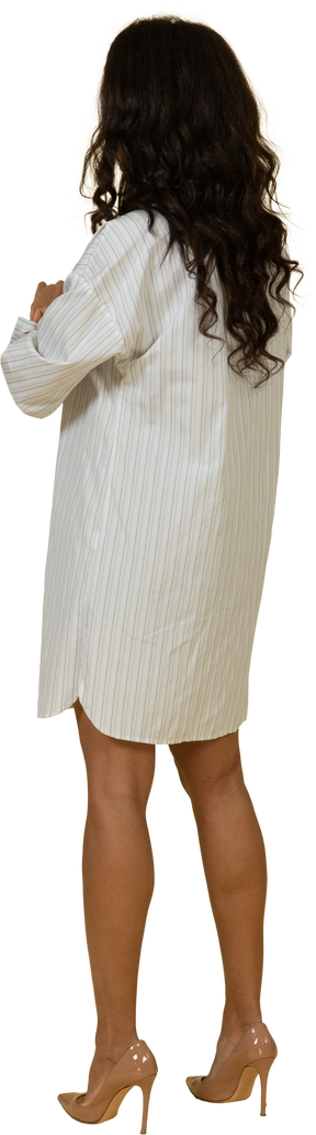 Vista posterior de tres cuartos de una mujer joven de piel oscura con vestido blanco arremangándose