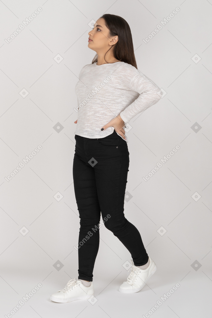 Three-quarter view of a young  indian female in casual clothes putting hands on waist