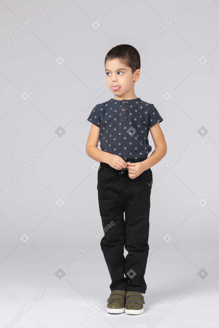Front view of a cute kid boy in casual clothes showing tongue and looking aside