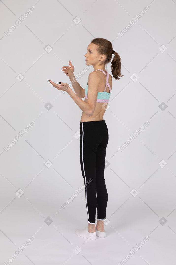 Vista posterior de tres cuartos de una adolescente en ropa deportiva levantando la mano y argumentando