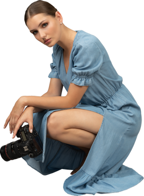 Vue latérale d'une jeune femme en robe bleue assise sur un sol avec appareil photo