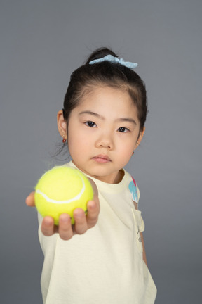 Niña ofreciendo una pelota de tenis