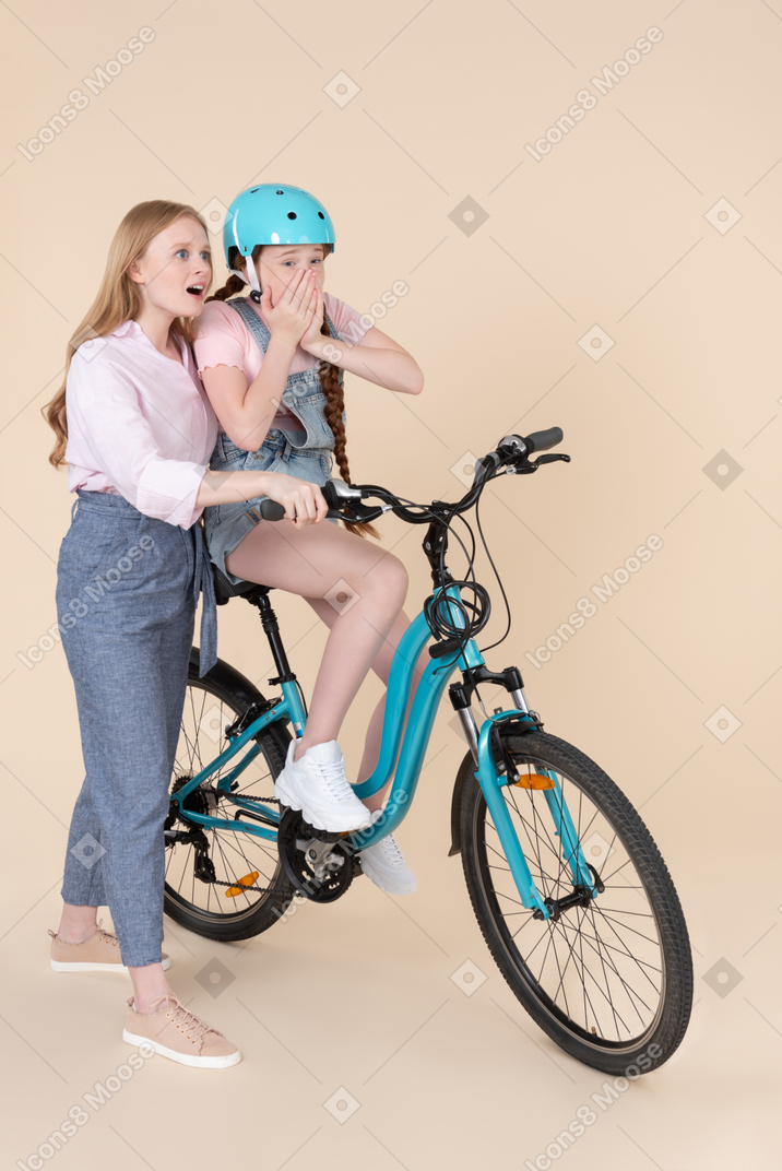 자전거를 타는 방법을 무서워하는 십 대 소녀를 가르치는 놀란 젊은 여자