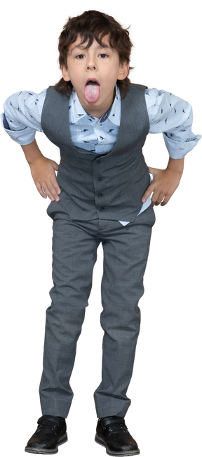 Vista frontal de un niño con traje gris posando con las manos en las caderas y mostrando la lengua