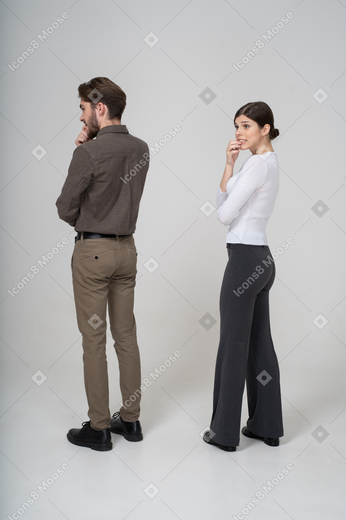 Three-quarter back view of a nervous young couple in office clothing touching chin