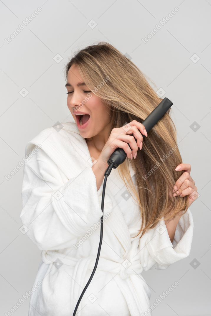 Beautiful young woman screaming while styling her hair with flat iron