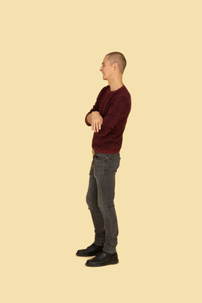 Side view of a displeased young man dressed in casual clothes crossing his hands