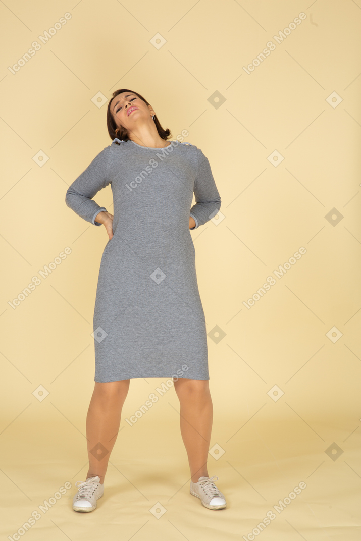 Vista frontal de uma mulher de vestido cinza sofrendo de dor nas costas