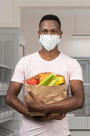 Man in face mask holding a bag of groceries