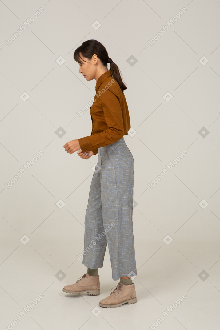 Vista lateral de uma jovem mulher asiática de calça e blusa, olhando para baixo