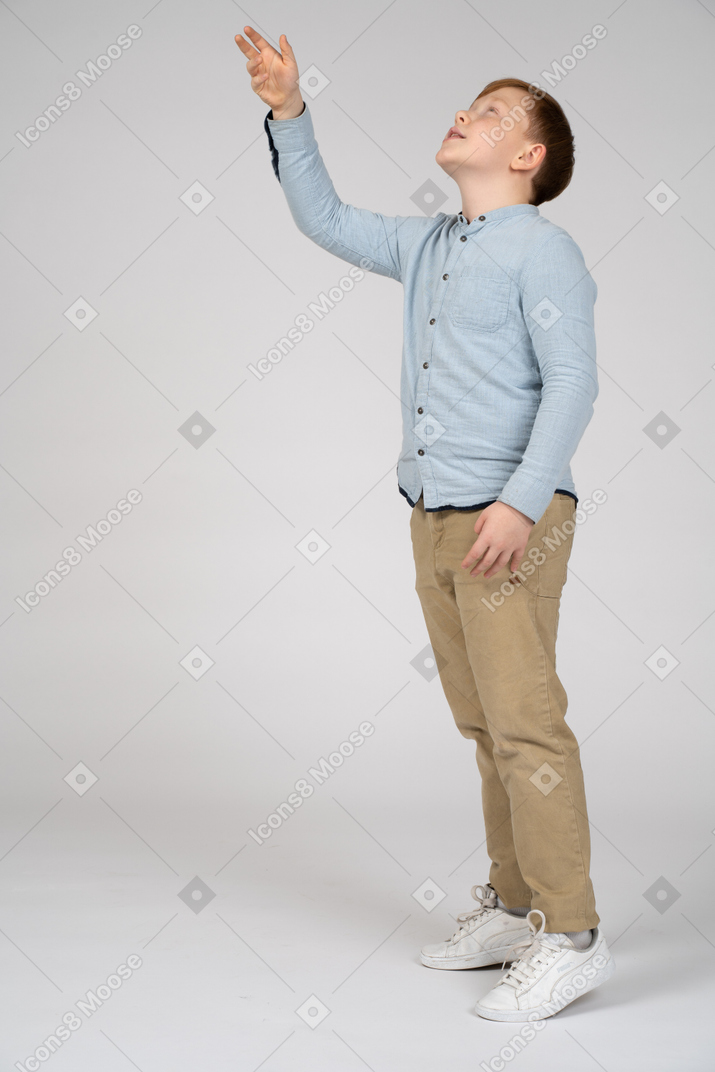 Вид сбоку на мальчика, указывающего вверх рукой