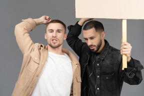 Close-up of two young men with a billboard looking agitated