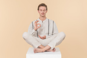 Young man sitting in lotus pose and showing ok sign