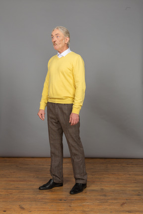 Three-quarter view of an old surprised man in yellow pullover looking aside and grimacing