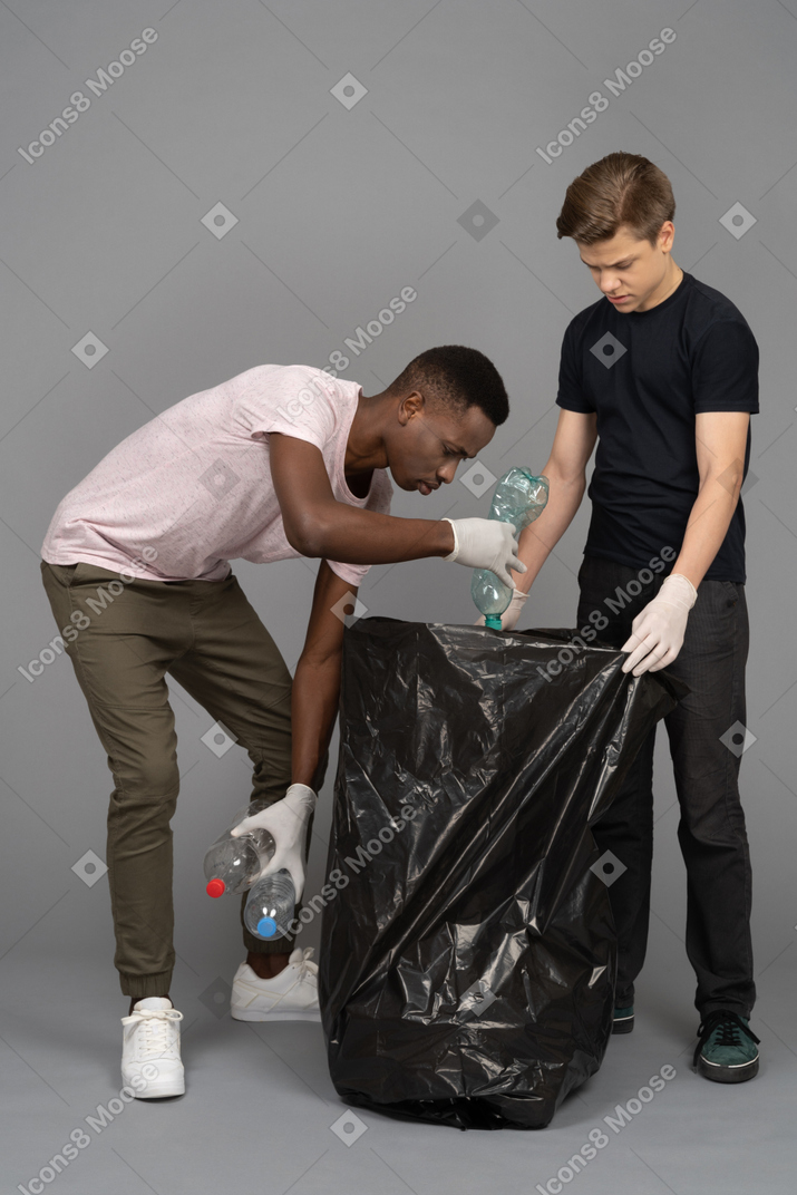 Young man helping his friend to put plastic bottles into a trash bag