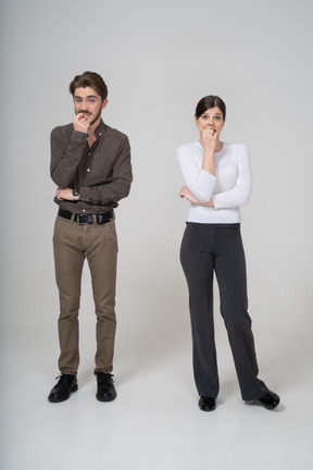 一对紧张的年轻夫妇在办公室服装触摸下巴的前视图