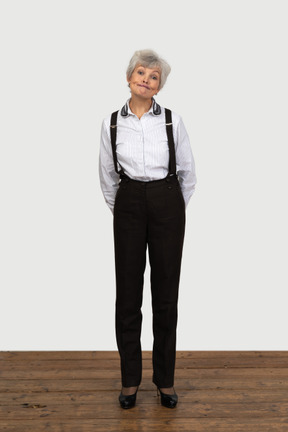 Front view of an old perplexed female in office clothes grimacing with her hands behind back