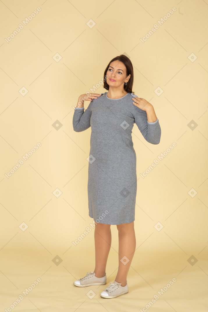 Front view of a woman in grey dress posing with hands on shoulders