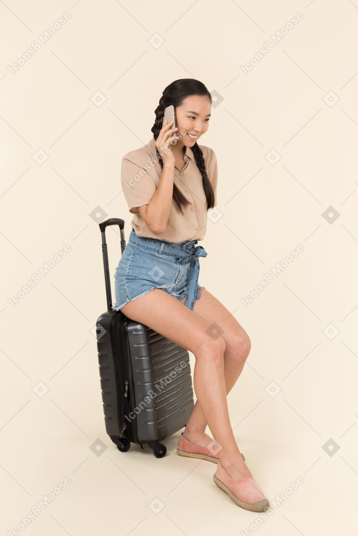 Smiling young female traveller sitting on suitcase