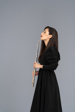 Vista laterale di una giovane donna seria in abito nero tenendo il flauto