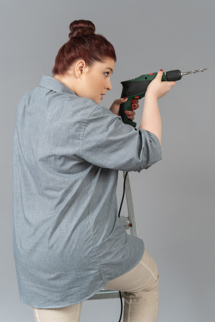 Young woman drilling a wall