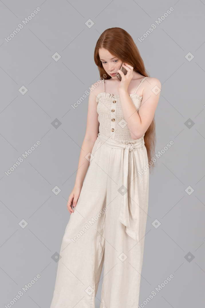 Teenage girl wearing beige overalls looking aside while talking on the phone