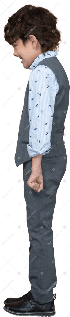 Vista lateral de um menino zangado em um terno cinza em pé com os punhos cerrados