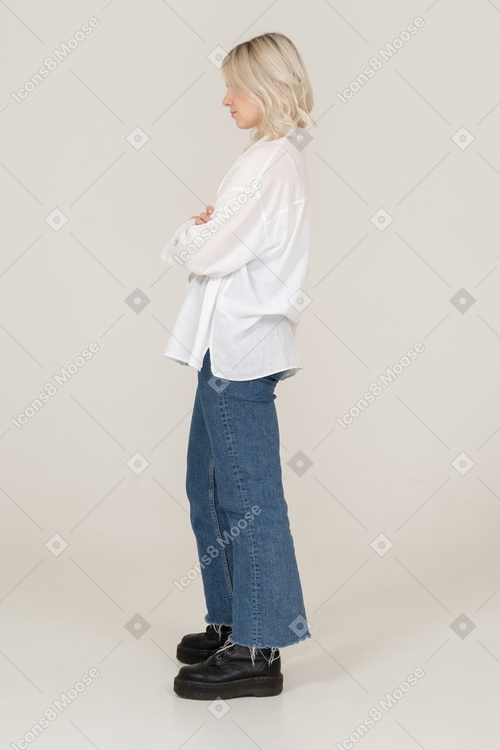 Seitenansicht eines weiblichen blonden modells in der freizeitkleidung, die hände kreuzt